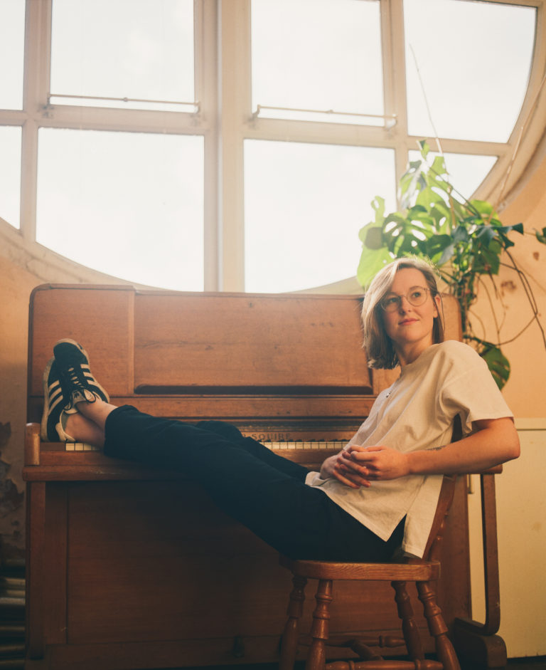 portrait of singer Lindsay Munroe sitting with feet on piano