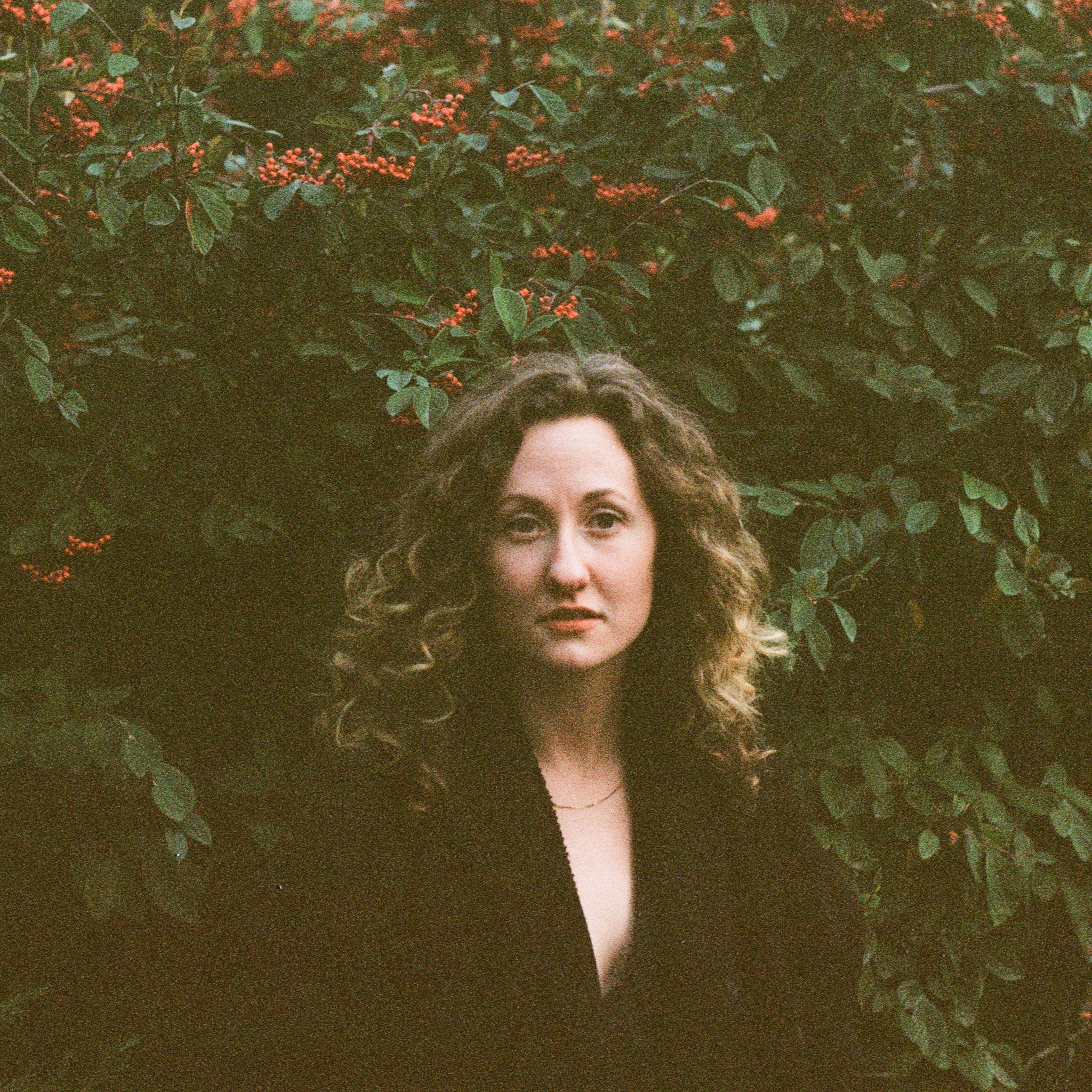 photo of corinne sharlet standing in front of green-leaved bushes