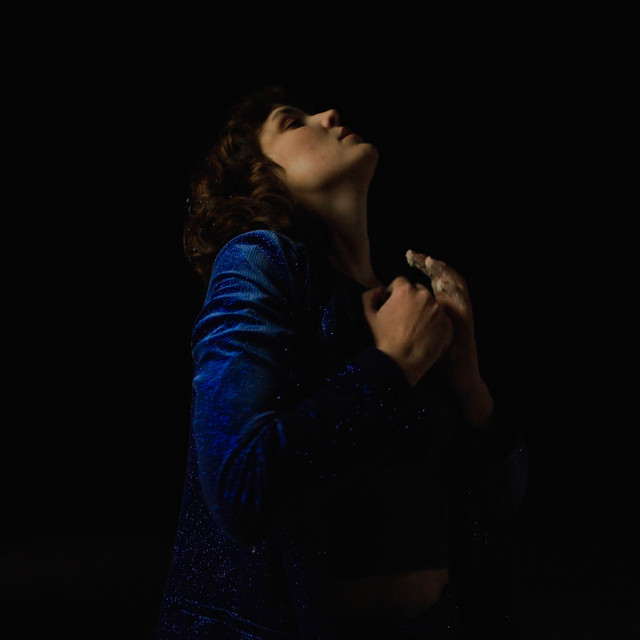 a picture of a woman, the songwriter Sophia Hansen-Knarhoi, wearing a sparkling blue jacket against a black backdrop