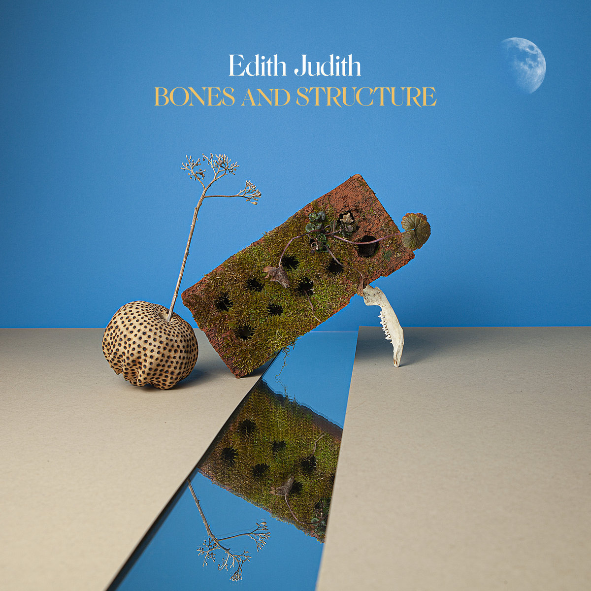 The artwork for Bones & Structure by Edith Judith featuring a mossy brick balance at a forty-five degree angle over a mirror against a blue background and a moon in the top corner
