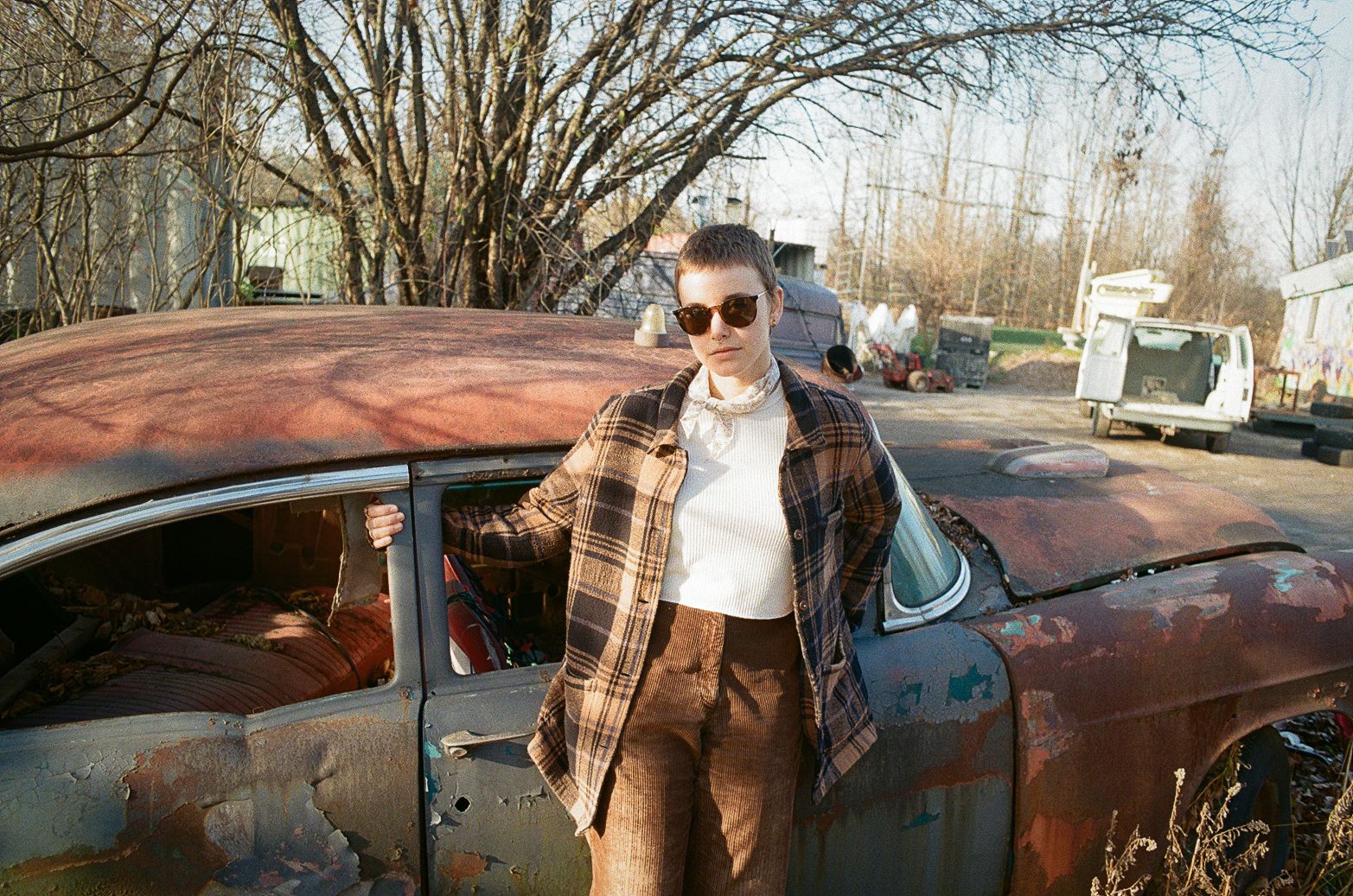 Cat Clyde portrait photo, standing next to a rusted old car and wearing sunglasses