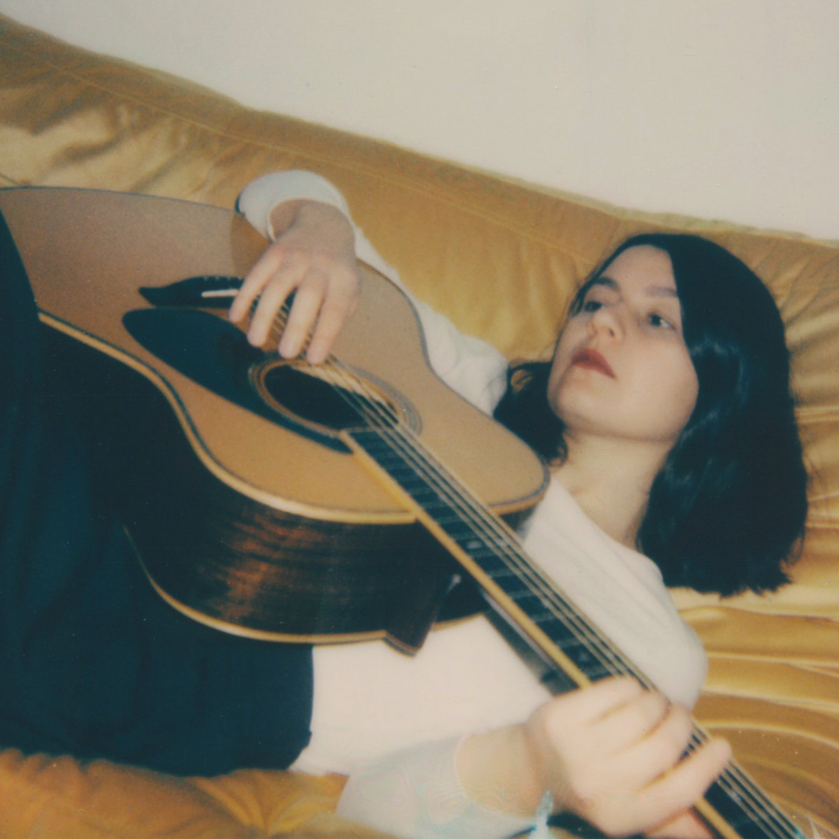 album art for Nothing's Set In Stone by Kraków Loves Adana, photo of lead Deniz Çiçek playing an acoustic guitar on a sofa