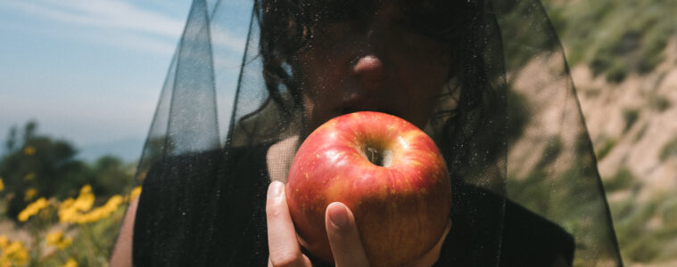 a picture of the artist Magana wearing a black veil eating an apple