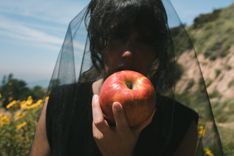a picture of the artist Magana wearing a black veil eating an apple