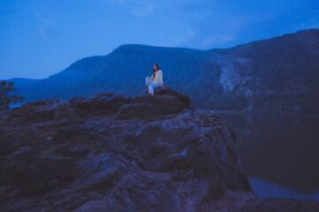 a picture of the songwriter Lea Thomas sitting on a rocky outcrop in a blue dusk light