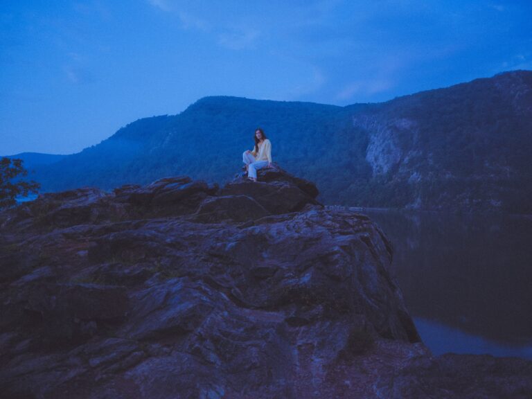 a picture of the songwriter Lea Thomas sitting on a rocky outcrop in a blue dusk light